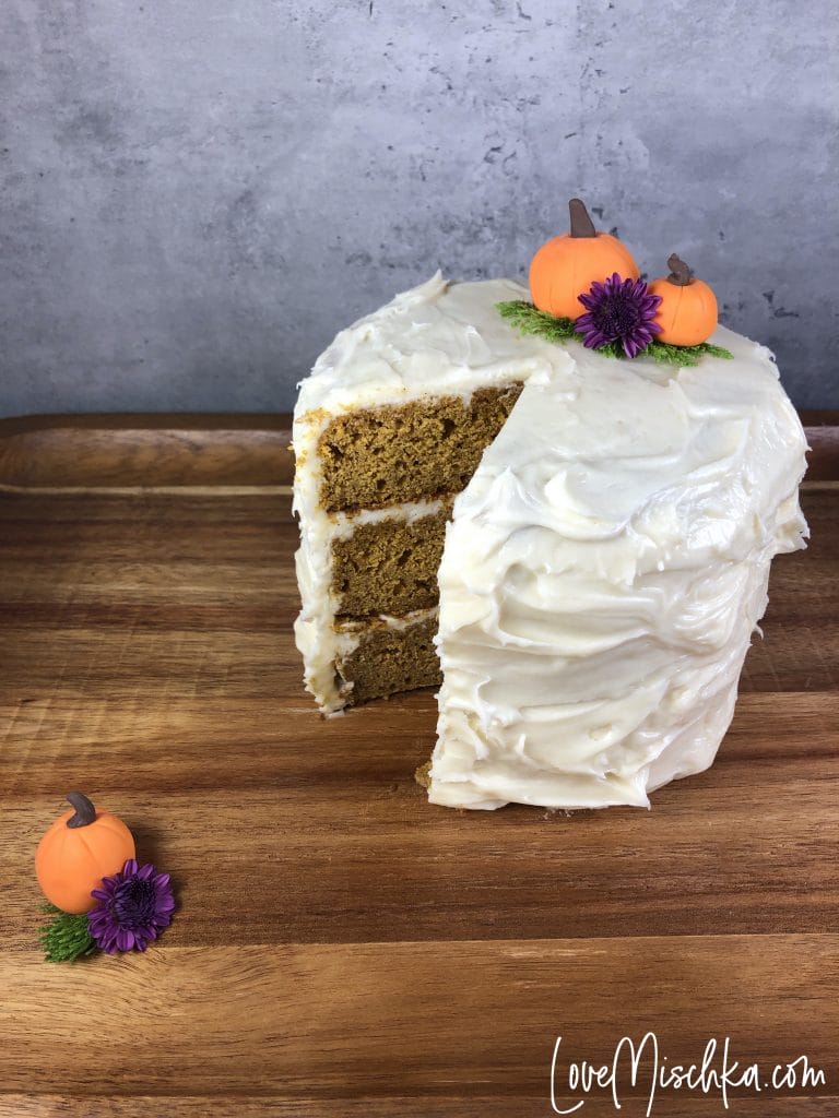 Tall Pumpkin Cake with a Slice Missing. Two Pumpkins on the cake and one on the wooden serving tray.